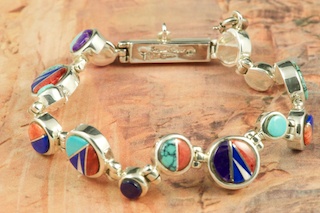Genuine Turquoise, Spiny Oyster Shell, Sugilite, Mother of Pearl and Blue Lapis inlaid between ribbons of Sterling Silver. Beautiful channel inlay design. Designed by Navajo Artist Calvin Begay. Signed. 
